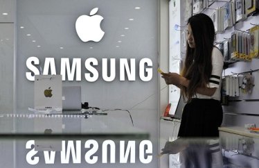 A sales assistant uses her mobile phone next to the company logos of Apple and Samsung at a store in Hefei, Anhui province in this September 10, 2014 file photo. Global smartphone leader Samsung Electronics Co Ltd is planning a new product launch next year based on its own Tizen operating system, the South Korean giant's strategic push to free itself from Android and blaze its own software path. But after years of development and a handful of Tizen-powered smartwatches and cameras, the only product confirmed for a 2015 launch so far is a TV set. REUTERS/Stringer/Files (CHINA - Tags: BUSINESS SCIENCE TECHNOLOGY)