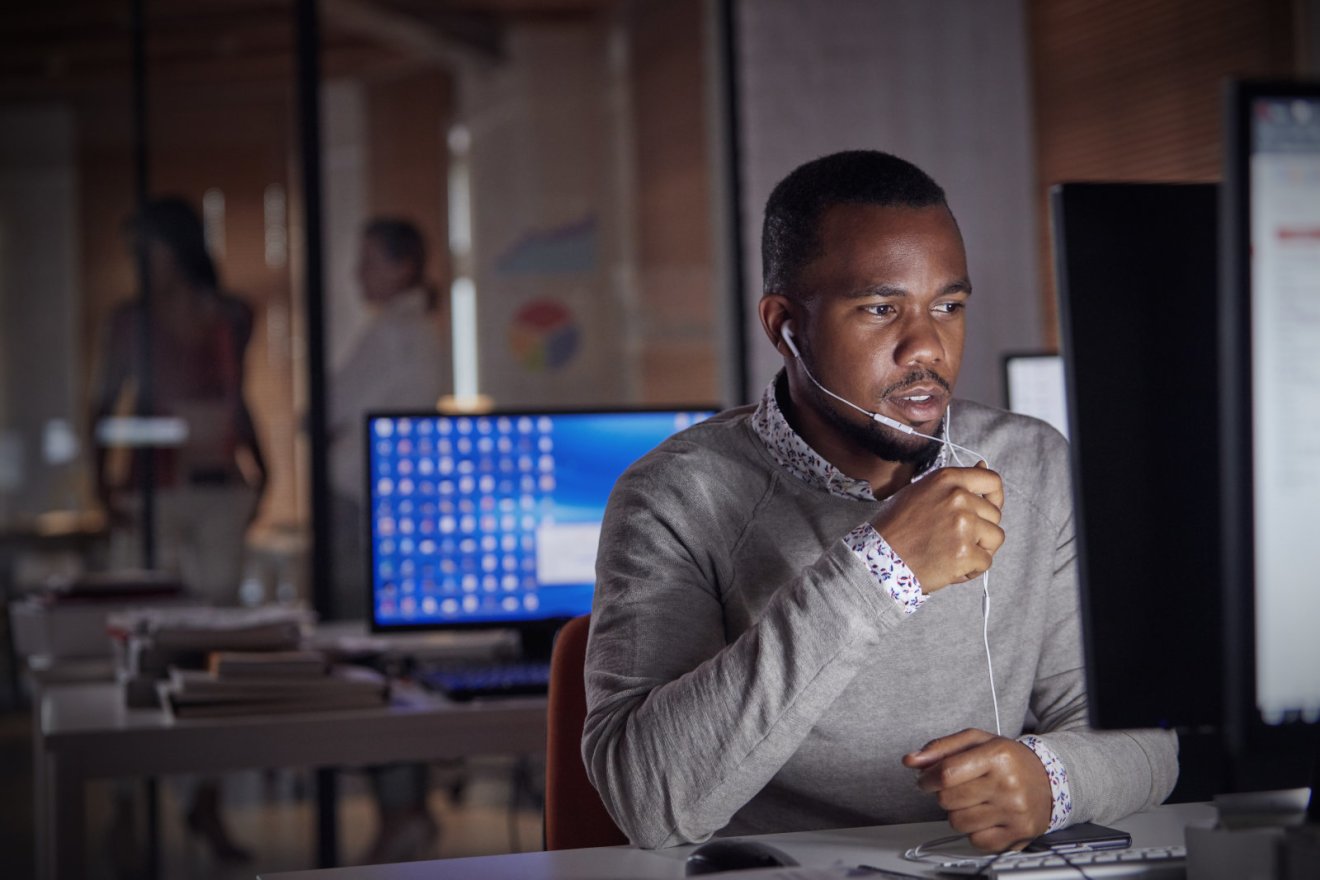 Businessman working late at computer, using hands-free headphones talking on telephone