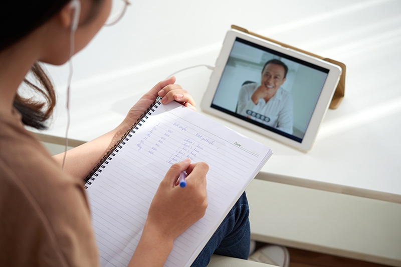 Female student watching online lesson and taking notes in textbook