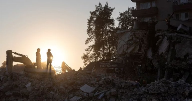 A search team dig through the rubble of a collapsed building with excavators