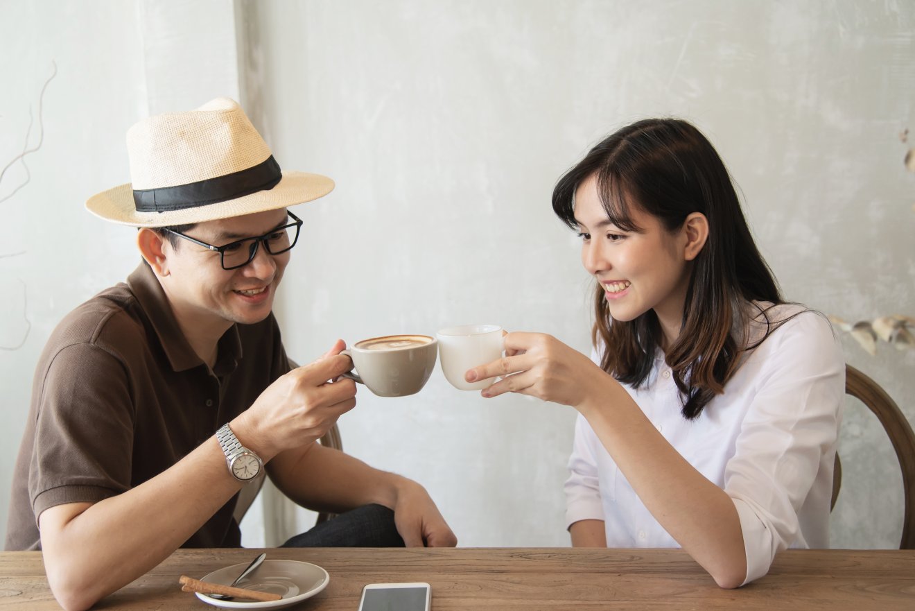 Casual man and woman talking happily while drink coffee and looking mobile phone - happy time lifestyle in coffee shop