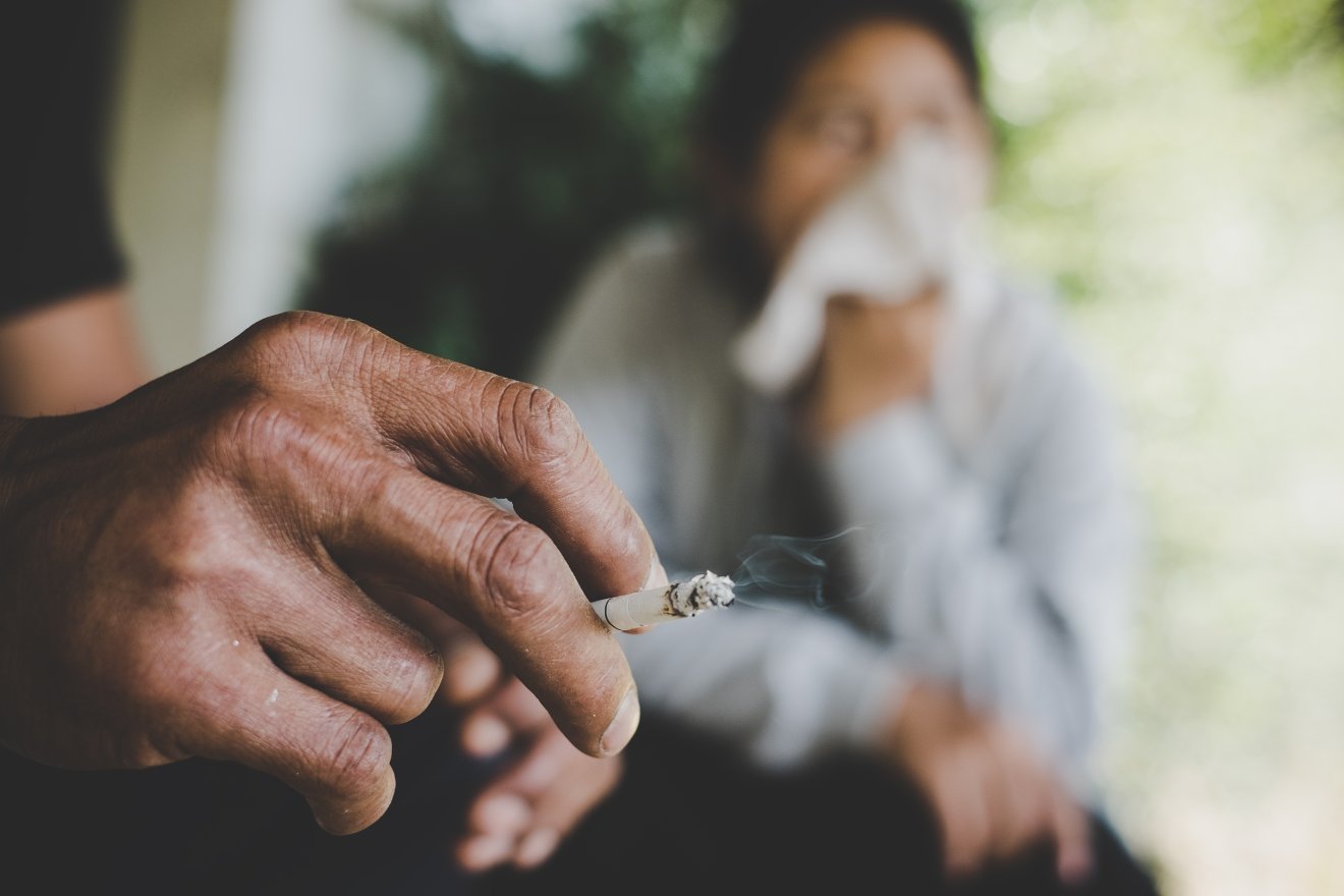 Image of cigarette is in the hand of man in the park.