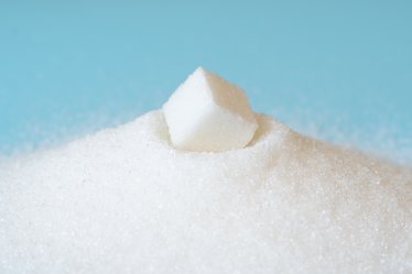 White sugar in bowl isolated on blue. a piece of refined sugar in a pile