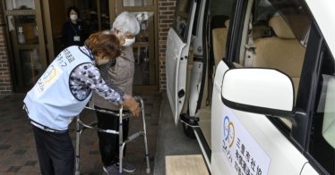 A staff member at a nursing home helps an elderly resident board a minivan