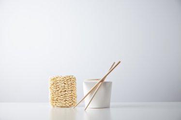 Brick of dry japanese noodles presented near closed blant retail takeaway box with chopsticks, isolated on white